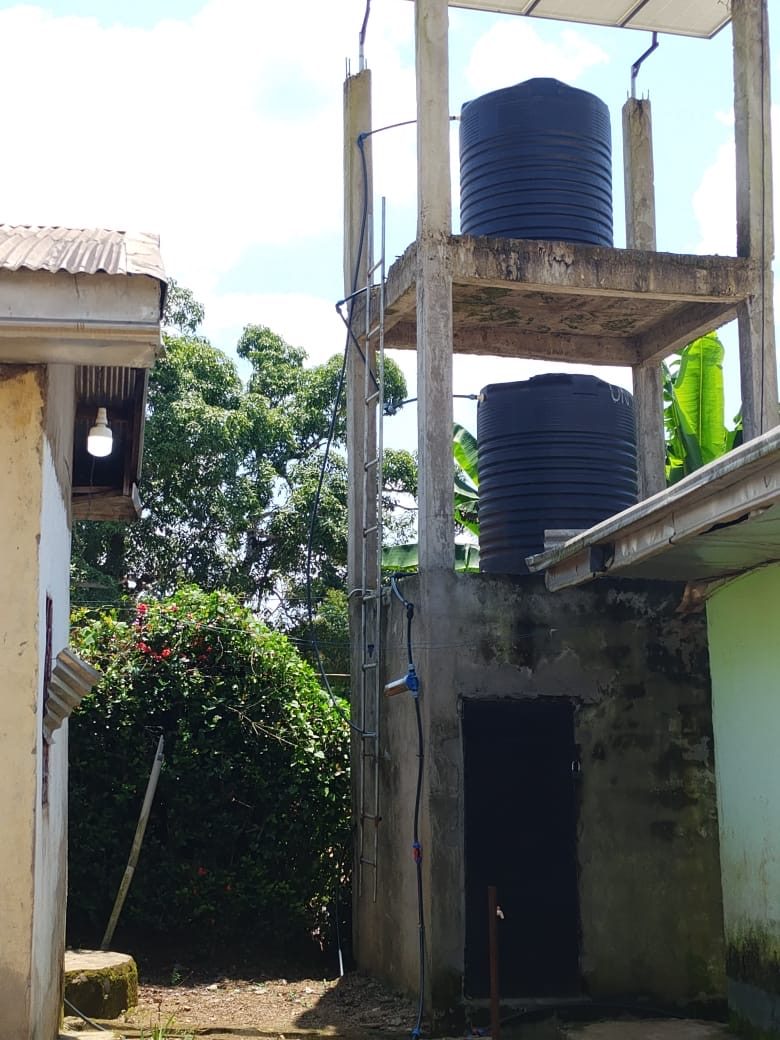 Two water storage tanks in place on the finished tower, with the pump housing and tap below